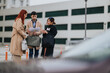 © qunica.com - Three business workers examine paperwork while standing near a modern office building. Colleagues review documents together outdoors in an urban setting.