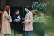 © qunica.com - Three business workers talk and share documents while standing outdoors. Colleagues discuss notes and ideas during a casual meeting by the office.
