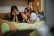 © qunica.com - Two women lie on a bed talking and relaxing in a casual bedroom setting. The friends chat and look at a phone while resting on a floral bedspread.