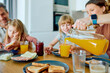 © we.bond.creations - Family enjoying morning breakfast, mother pouring orange juice for her daughter as father and other child are watching