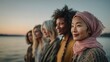 © rabbit75_fot - Female diversity. Human rights, equal opportunity concept. A portrait of four women standing by a lake during sunset. The setting sun casts a warm orange and pink hue over the scene.