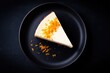 © Ziyad - A single slice of cheesecake, topped with orange zest, sits on a dark plate, isolated on black