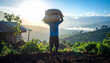 © YSMR2000 - Back View of Man Carrying Heavy Harvest Sacks on Head Overlooking Rural Kenyan Farmland at Morning