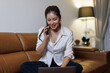 © David - A young woman sits comfortably on a sofa, smiling while on a call, showcasing the ease of remote communication and the blend of personal and work life in a cozy setting.