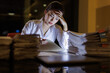 © David - A focused businesswoman is seen in a dimly lit office, overwhelmed by paperwork and showing signs of stress and fatigue as she tries to manage her workload effectively.