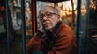 © Po - An elderly man with glasses and a beard rests his head on his hand, looking thoughtful by a window during sunset.