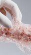 © dinatychynska - Gloved scientist stretching transparent artificial skin biomaterial mesh with porous cellular network structure, engineered for medical prosthetics transplantation and human tissue regeneration.