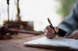 © MINAE - Lawyer hand writing on an important legal document or contract, with a blur of a gavel and scales of justice on a wooden desk, symbolizing the legal profession and business law