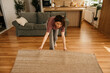 © La Famiglia - Woman unrolling rug on wooden floor in apartment