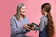 © New Africa - Little girl greeting her grandmother with gift on pink background
