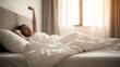 © TRIMAH - Person waking up in a bright bedroom, stretching under white bedding near a sunny window