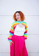 © VISTA by Westend61 - Happy woman in colorful rainbow sweater and pink skirt smiling outdoors