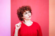 © VISTA by Westend61 - Curly redhead in red sweater thinking with pencil against vibrant background