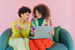 © VISTA by Westend61 - Two friends with curly hair using laptop and smiling on sofa indoors