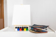 © anivvelia - Blank canvas on easel with painting supplies on white table, minimal art workspace with copy space