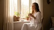 © dreamdes - Woman sitting by window drinking tea. Young girl enjoying peaceful morning with hot cup of tea. Relaxed lifestyle concept at home. Sunlight streaming through curtains during quiet cozy break