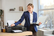 © Pixel-Shot - Young businesswoman with laptop using printer in office