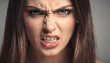 © Oleksandr - Intense close-up of a young woman's face, her brow furrowed and teeth bared in an expression of extreme anger, frustration, or disgust against a grey background