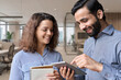 © insta_photos - Diverse friendly coworkers colleagues indian male manager and latin female employee talking in office using tablet device, having fun and laughing together discussing project.