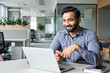 © insta_photos - Happy smiling ethnical indian businessman having online virtual meeting call on laptop looking at screen sitting at table in coworking creative office, professional manager talking to employees.