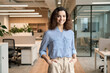 © insta_photos - Young smiling latin girl college student or teacher looking at camera standing in university campus. Happy hispanic millennial woman professional posing in modern coworking creative office space.