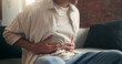 © peopleimages.com - Man, hands and sick in home with stomach ache, indigestion and inflammation from diarrhea problem. Person, abdomen pain and medical issue on couch with constipation, bowel discomfort and bloating.