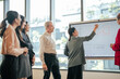 © Wanwajee - Business team gathers around presenter explaining data insights on whiteboard in modern office. Group discussion supports better decisions. Concept of teamwork and strategy.
