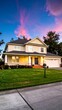 © Tas - Two-story house with a green lawn. Blue door, white trim, and a garage are visible. The sunset creates a dramatic sky backdrop