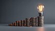 © tur - Illuminated incandescent bulb rests atop the tallest stack of metallic currency in a rising progression
