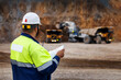 © Parilov - Engineer worker supervisor in high visibility jacket and helmet reviewing plans and work of truck at open pit mine for safety briefing