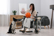 © New Africa - Woman in wheelchair with basketball ball and her service dog indoors