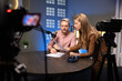 © fizkes - Two focused podcasters collaborating in studio, reviewing documents, analyzing data, discussing episode script before recording content. Professional workflow in podcast production, media broadcasting