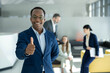 © Dejan - Smiling corporate professional making a positive gesture in modern office with diverse colleagues, representing teamwork and achievement