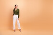 © deagreez - Confident businesswoman in green blouse and white pants poses against warm beige backdrop