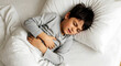 © NUR - Young boy in bed holding stomach in pain with eyes closed child sick