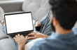 © Prostock-studio - Indian Man Using Laptop Computer With Blank White Screen While Sitting On Couch At Home, Unrecognizable Guy Working Online Or Browsing Internet Website, Over Shoulder View, Mockup With Copy Space
