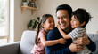 © yoga - Happy Southeast Asian father laughing while being hugged by his two young children on a sofa at home, candid family bonding moment.