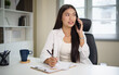 © matinee - Smiling female entrepreneur having a phone conversation at her desk with laptop.