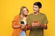 © ViDi Studio - Young smiling happy satisfied couple friends family man woman wear casual clothes hold in hand use mobile cell phone together isolated on pastel plain light yellow color background studio portrait