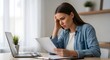 © DhimasPratama - A stressed woman sitting at a desk looking at a piece of paper