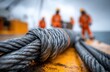 © NovaVision - Heavy duty steel cable secured with a knot on a yellow surface with workers in orange suits in background