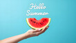 © Ruslan - A woman's hand holds a juicy watermelon slice against a blue studio background with the inscription 'Hello Summer' – a minimalist creative composition with copyspace for design