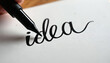 © Pete - Calligraphy pen writes word idea in elegant script on white paper. Black ink flows creating artistic lettering. Close up shot of creative process for new thought.