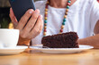 © luciano - Close up of senior woman relaxing for a break at coffee shop in mall using mobile phone enjoying a coffee cup and a slice of cake.
