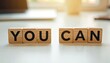 © Viktor - Wooden blocks with letters spell out YOU CAN on a white desk. This image promotes motivation and belief in ones ability to achieve goals. Positive affirmation for success and personal growth.