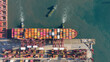 © AmazingAerialAgency - Aerial view of Kwai Tsing Container Terminal V with a large container ship docked under red gantry cranes and tugboats in the water Hong Kong, New Territories, Hong Kong.