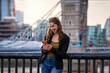 © moofushi - A fashionable, urban woman looks at her mobile phone in front of the city skyline of London