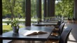 © Wuttichai - An open book and a potted plant rest on a table in a modern study hall with large overlooking a lush park