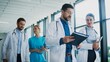 © VAKSMANV - Medical staff walking through bright clinic hallway talking with each other. Focused male doctor reviewing notes while colleague discuss plan. Nurse joining conversation and sharing thoughts.