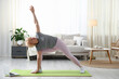 © New Africa - Senior woman practicing yoga via video chat with online coach at home, space for text. Fitness and sport